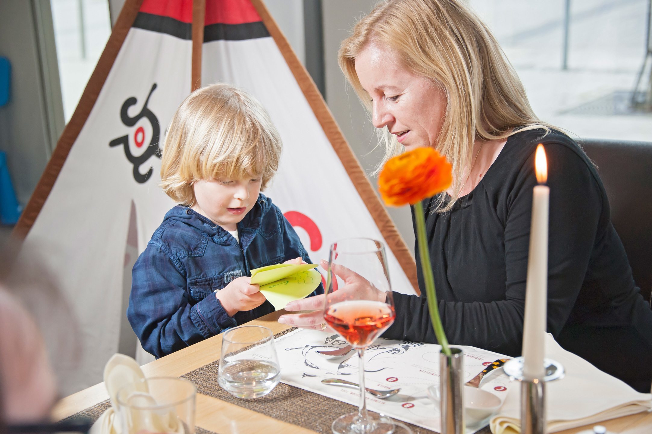 Mutter mit Kind im ATLANTIC Hotel Kiel Erwachsene und Kind basteln am Tisch im ATLANTIC Hotel Kiel, im Hintergrund ein Zelt.