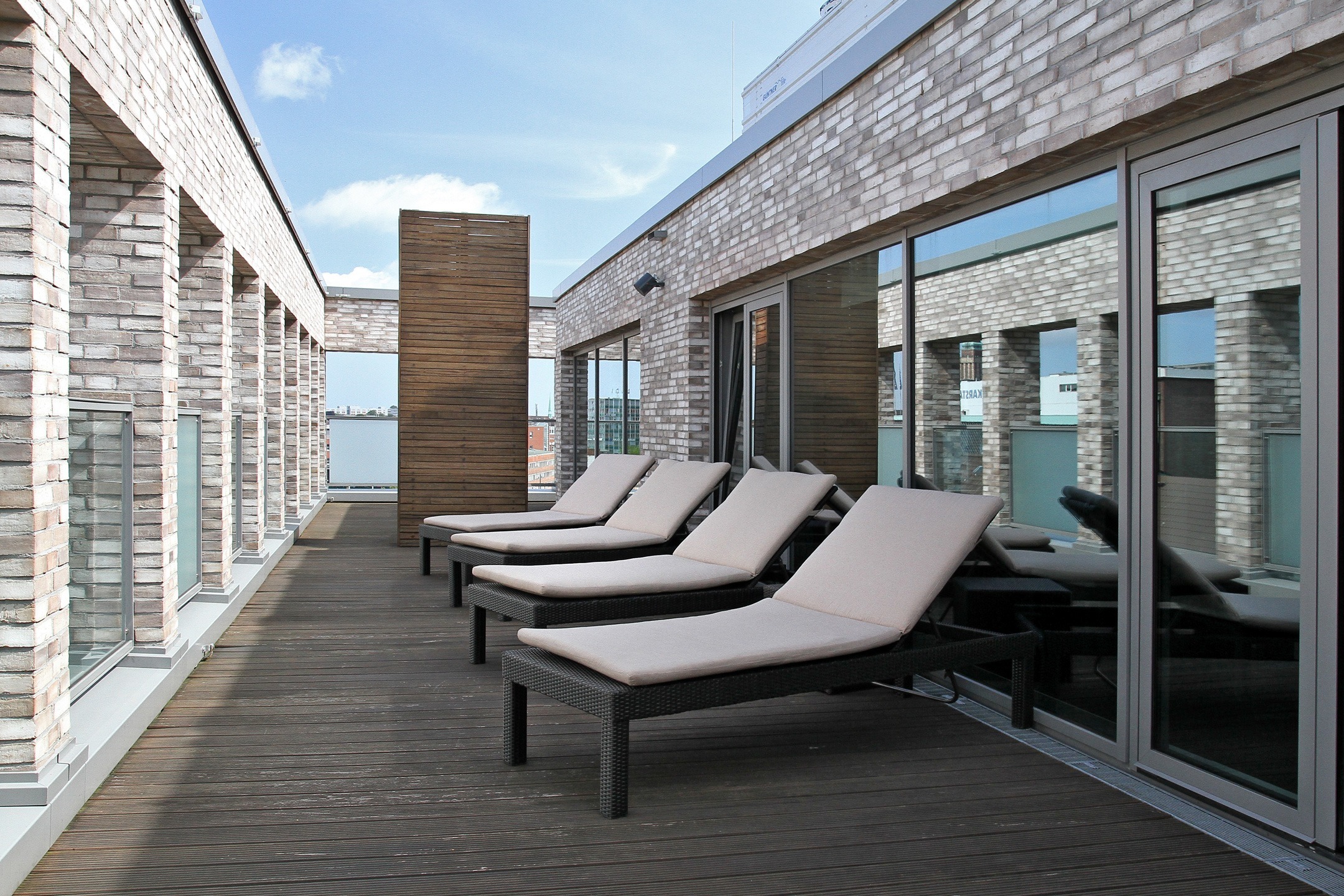Sun terrace of the ATLANTIC Hotel Kiel with sun loungers, wooden floor and brick walls under a blue sky.