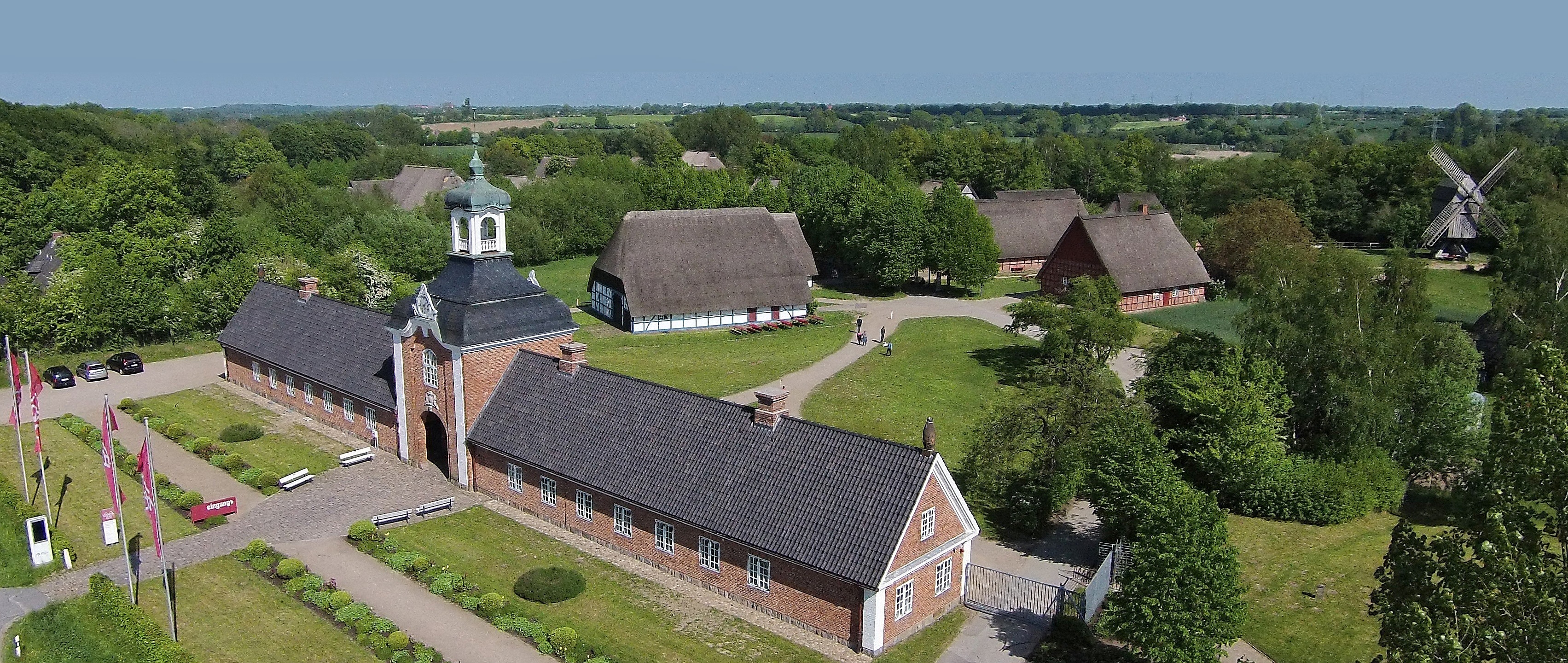 Terrain of the outdoor museum Wolfsee photographed for a bird's eye view Historic brick building with tower, surrounded by green countryside and traditional thatched roof houses.