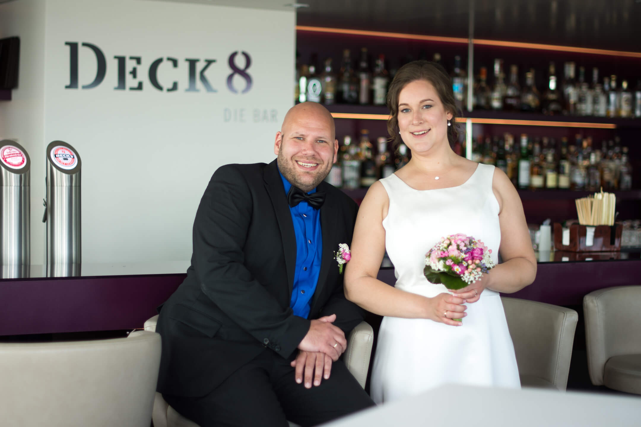 Paar in festlicher Kleidung in der Bar Deck 8 des ATLANTIC Hotels Kiel, umgeben von Getränken und Dekorationen.
