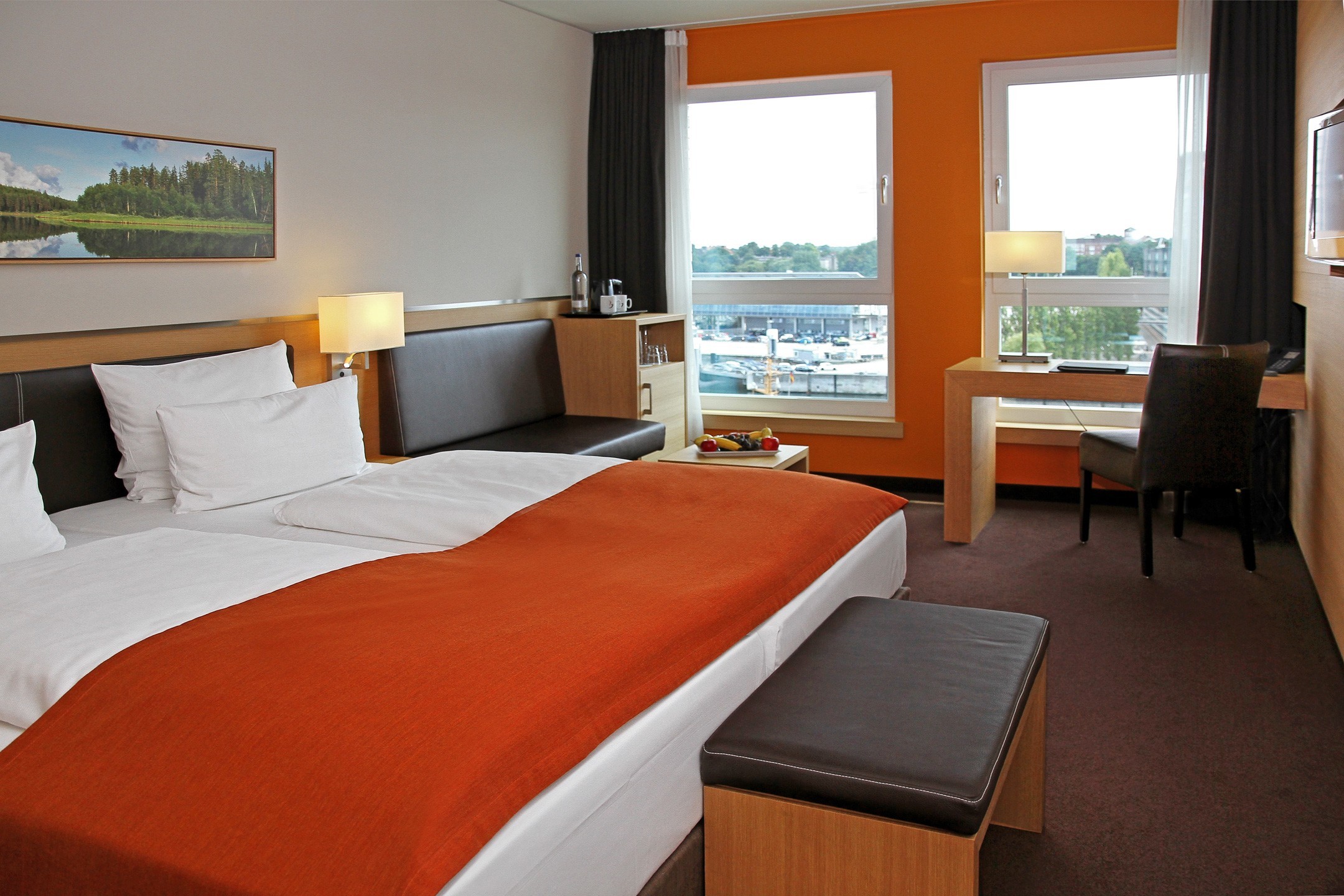 Modern hotel room at the ATLANTIC Hotel Kiel with double bed, desk, armchair and view of the harbor.