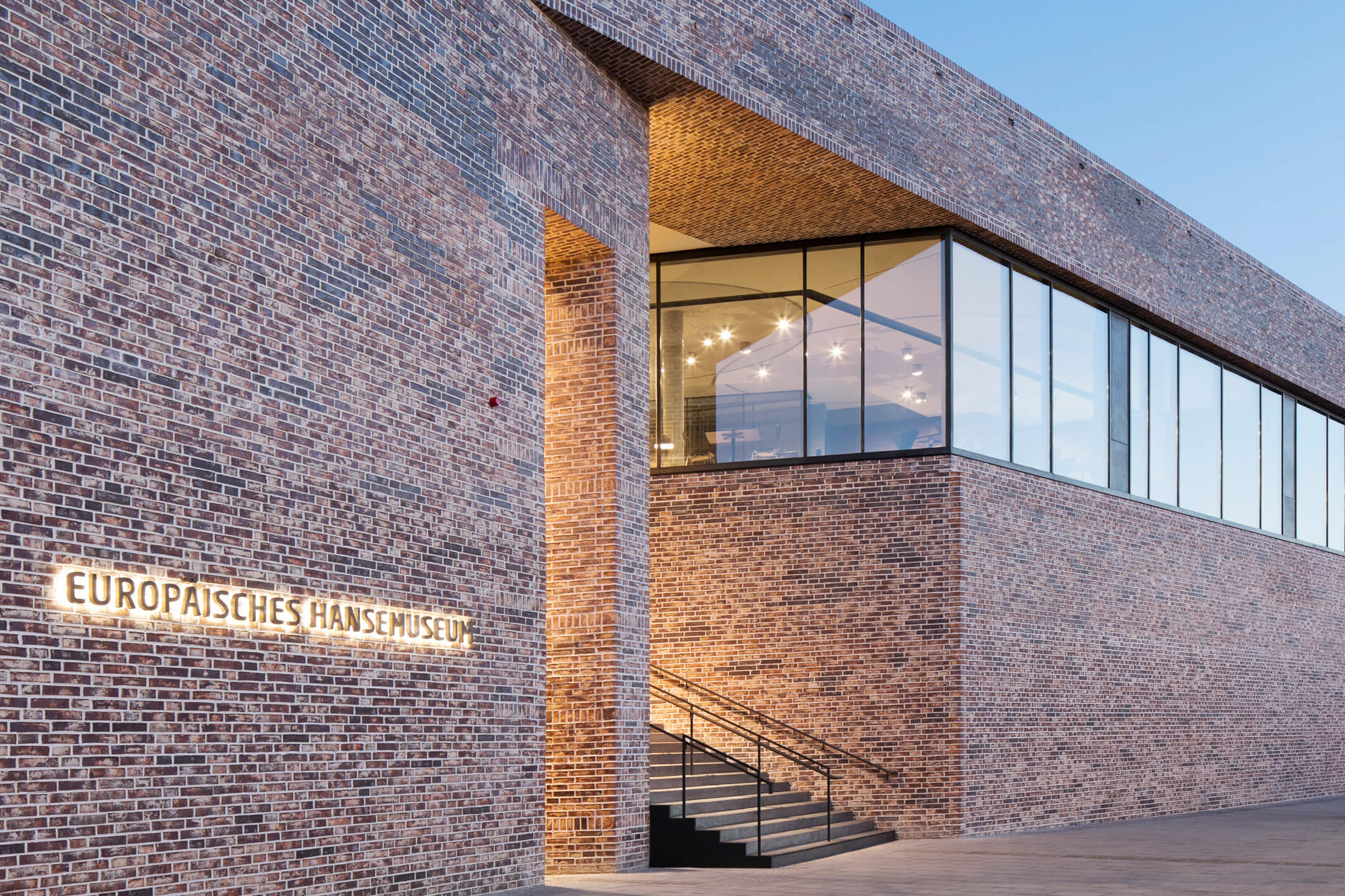 Brick building of the European Hanseatic Museum with illuminated entrance and large windows at dusk.