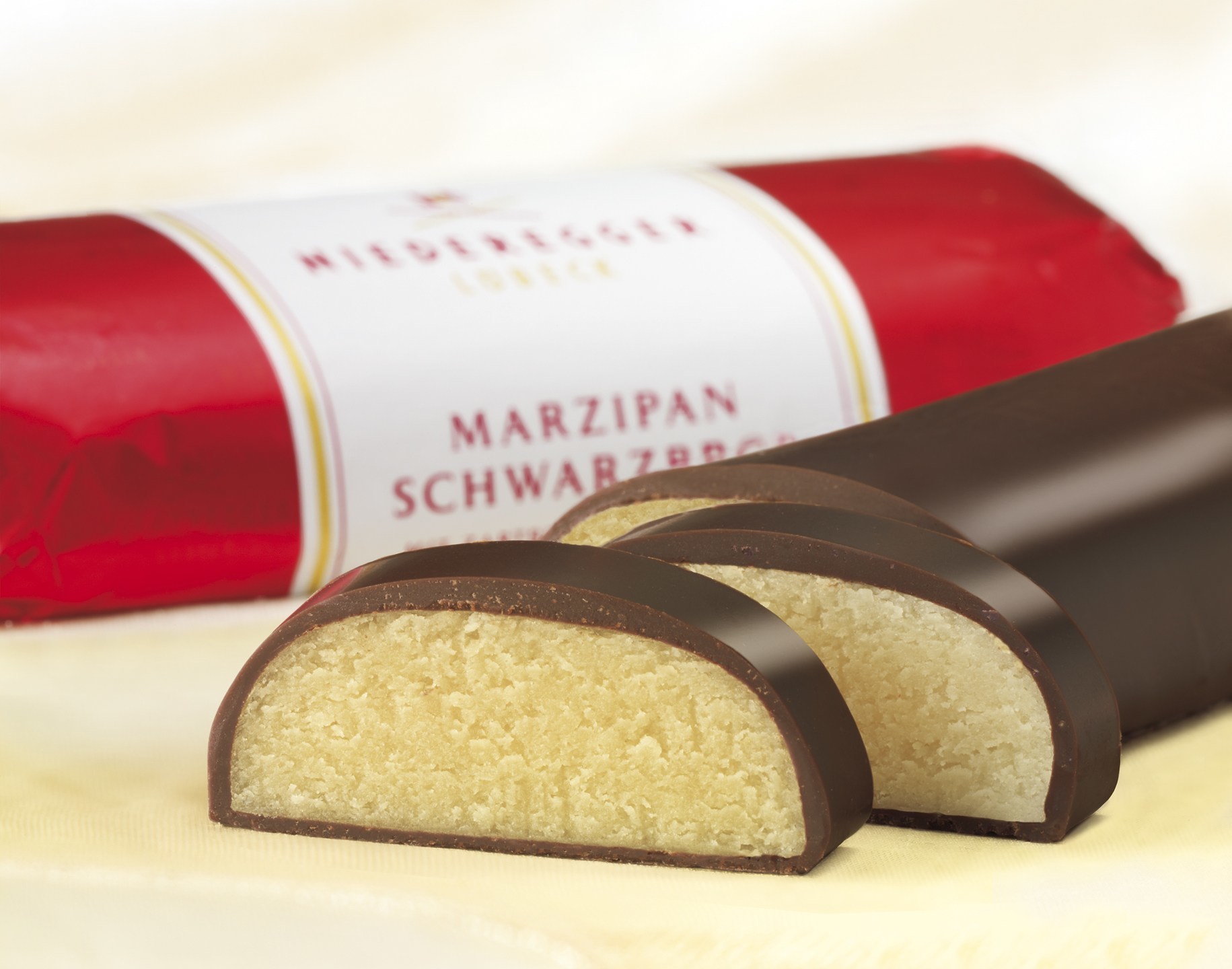 Geschnittenes Marzipan von Niederegger Niederegger Marzipan in Schokolade, teils aufgeschnitten, auf hellem Hintergrund präsentiert.