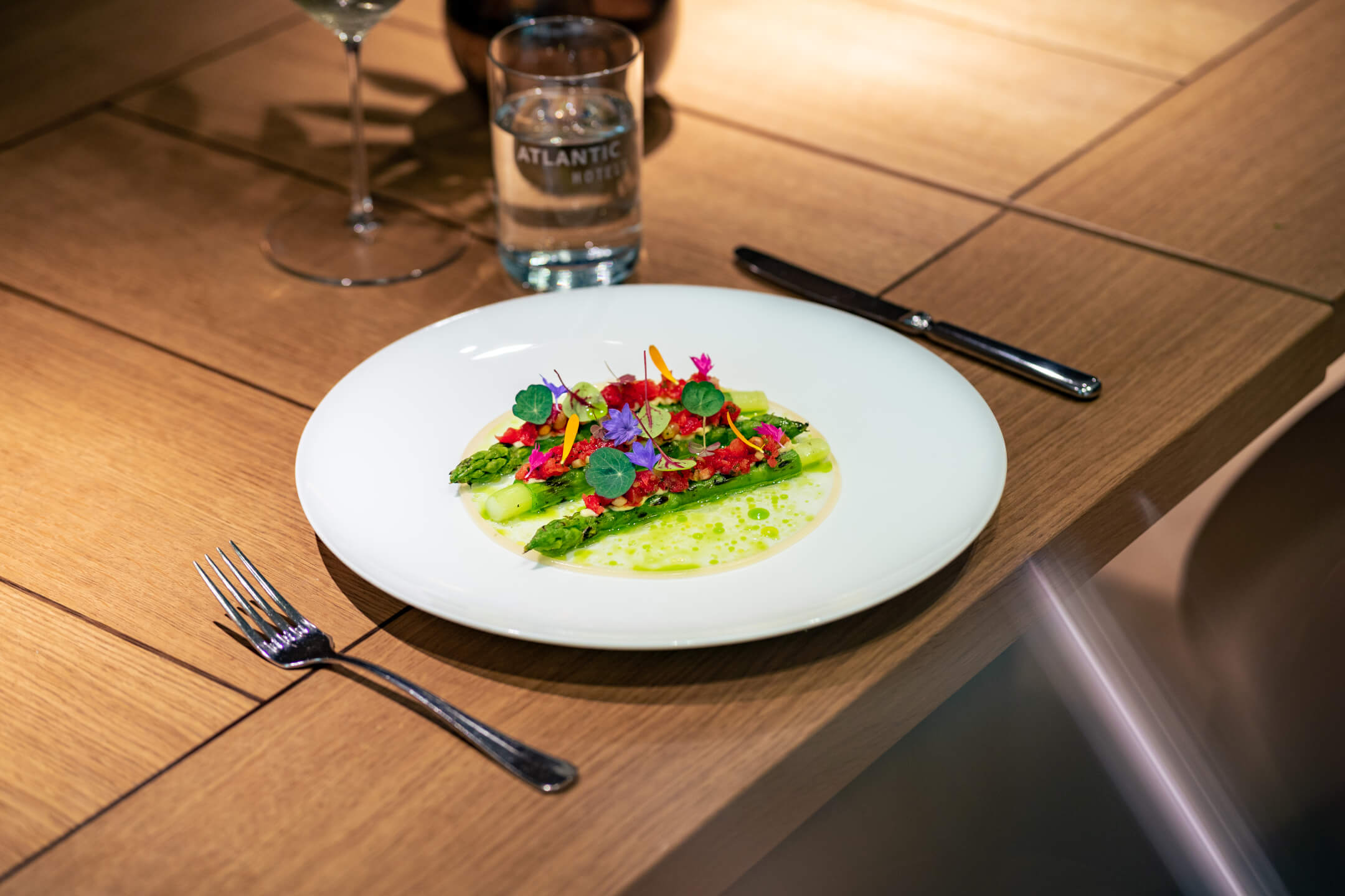 Restaurant ATLANTIC Grillroom | ATLANTIC Hotel Münster Ein kunstvoll angerichteter Salat mit Spargel und Blüten auf einem weißen Teller im ATLANTIC Hotel Münster.
