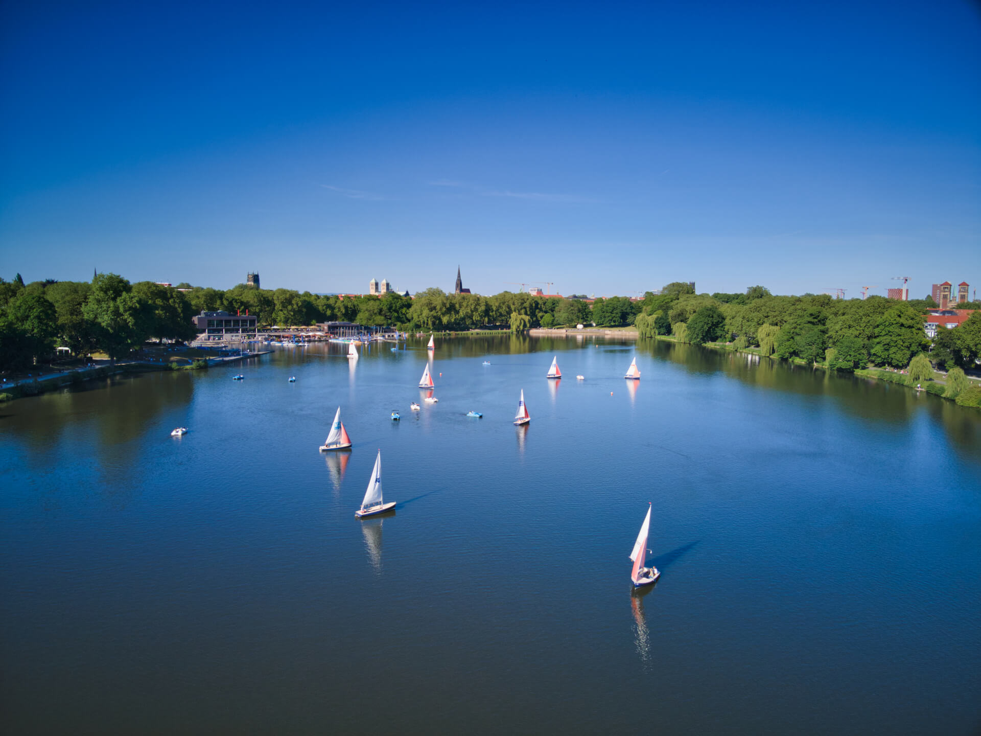 Recreation area Aasee in Münster Sailing boats on the Aasee in Münster, surrounded by green trees and a blue sky.