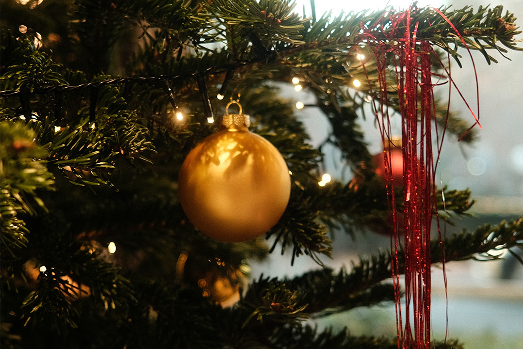 Nahaufnahme eines Weihnachtsbaumes mit Lichterkette, rotem Lametta sowie goldenen und roten Christbaumkugeln