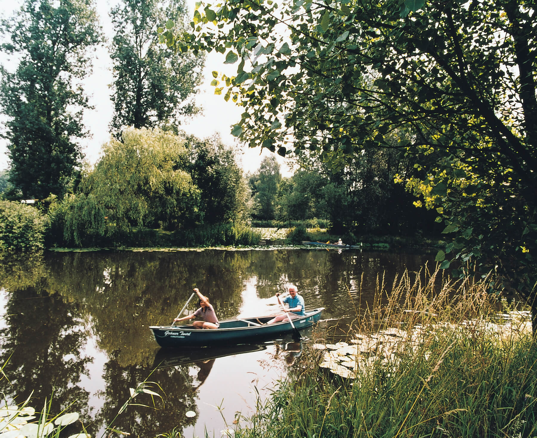 Local recreation area Rieselfelder Two people paddle in a canoe on a calm lake surrounded by trees.