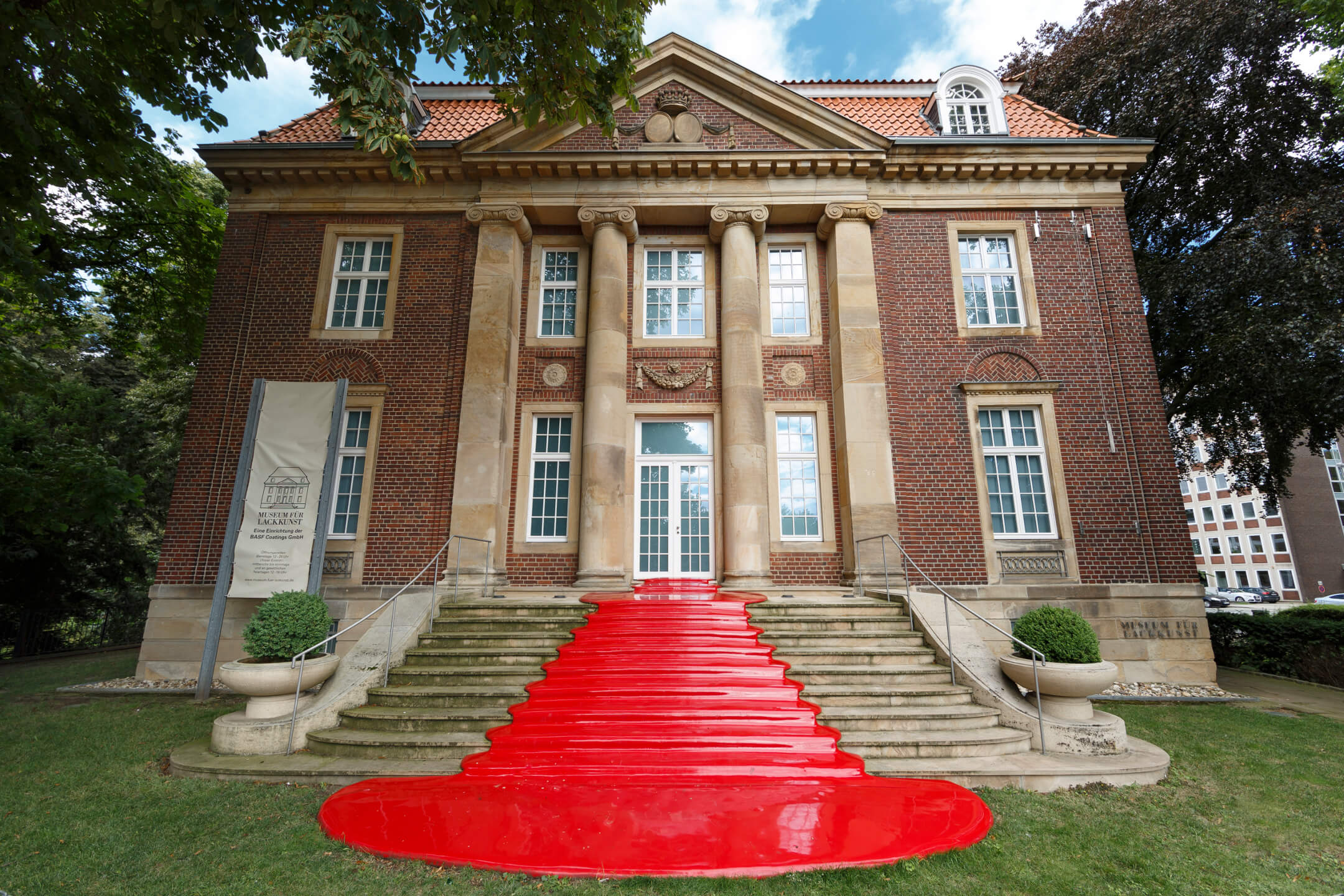 Museum of lacquer art Historic building with a red carpet on the staircase, flanked by columns and green plants.