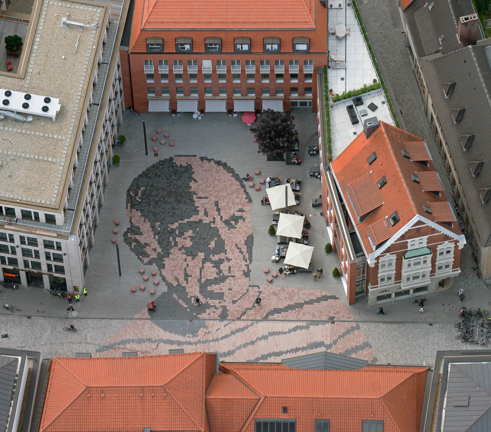 Pablo Picasso museum of art Aerial view of a square with a large cobblestone mosaic, surrounded by buildings with red roofs and outdoor terraces.