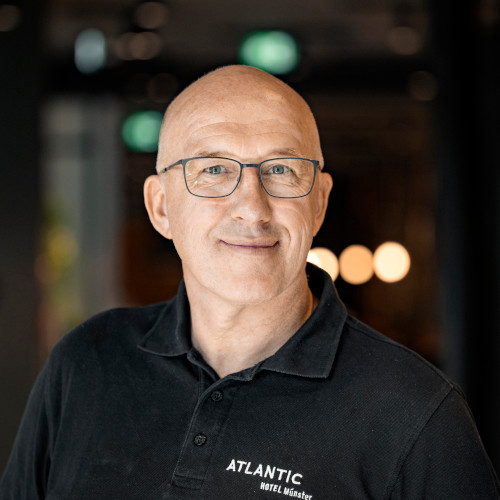 Eine Person in einem ATLANTIC Hotel Münster Polohemd lächelt in die Kamera.