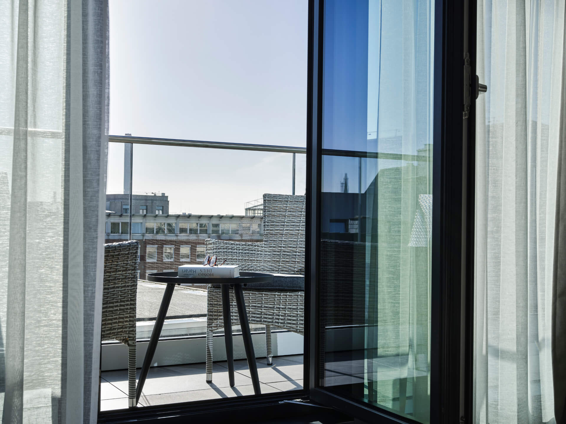 Blick von einem Hotelzimmerbalkon mit Glasgeländer, Tisch, zwei Stühlen und städtischer Aussicht im ATLANTIC Hotel Münster.