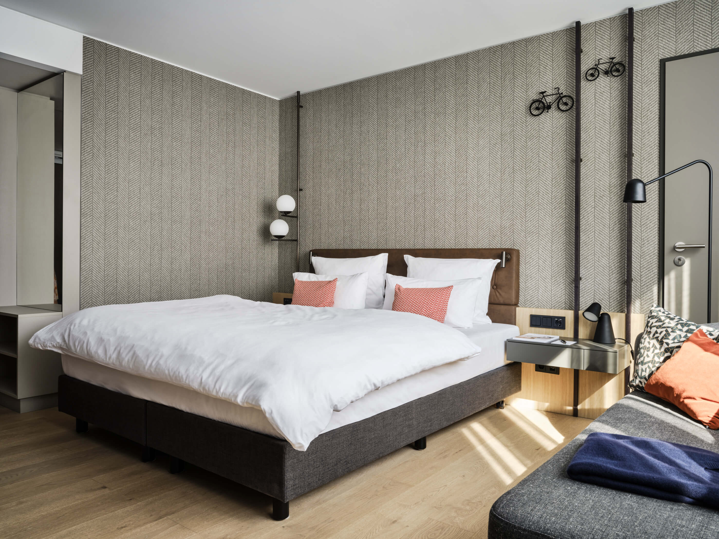 Modernes Hotelzimmer mit Doppelbett, stilvoller Beleuchtung, eleganter Tapete und dekorativen Fahrradmotiven an der Wand.