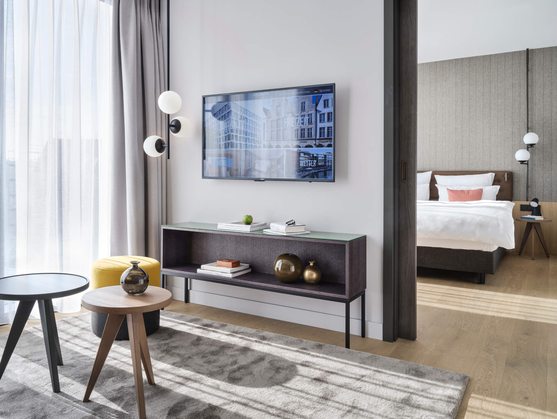 Modernes Hotelzimmer mit Doppelbett, Fernseher, dekorativen Tischen und hellem Vorhang im ATLANTIC Hotel Münster.