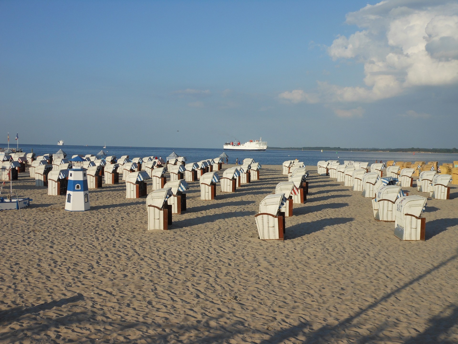 Strand mit vielen Strandkörben, Blick auf die Ostsee und ein vorbeifahrendes Schiff bei sonnigem Wetter.