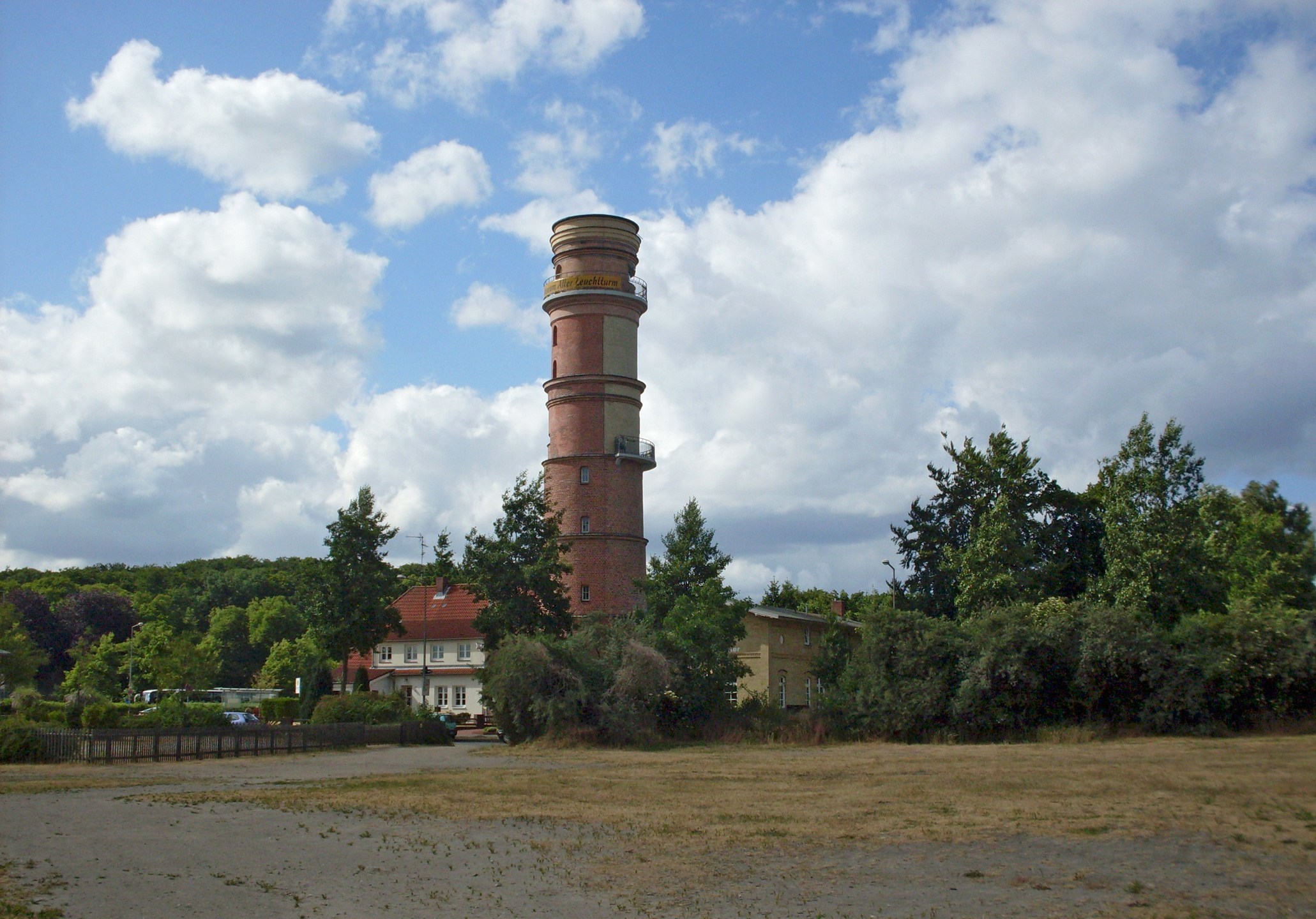 Roter Leuchtturm umgeben von Bäumen und Wolkenhimmel in Travemünde.