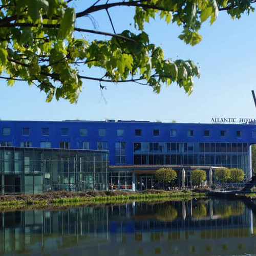 Außenansicht des ATLANTIC Hotel Universum in Bremen, am Wasser gelegen, mit moderner Glasfassade und blauen Akzenten.