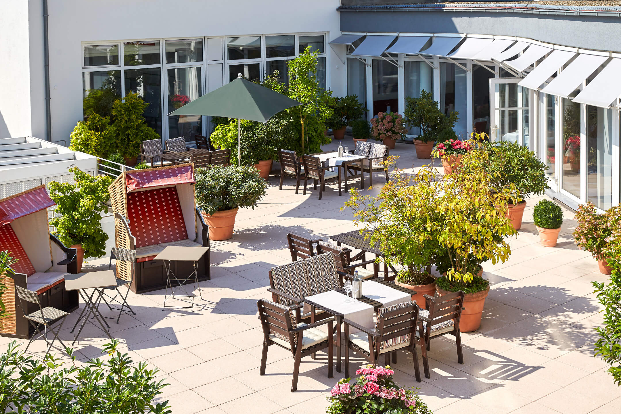 Sonnige Hotelterrasse mit Strandkörben, Tischen und Pflanzen im ATLANTIC Hotel Vegesack in Bremen.