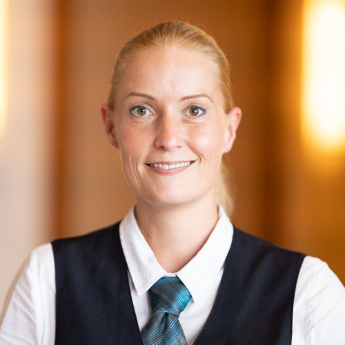 A smiling hotel employee in uniform in front of a blurred background.