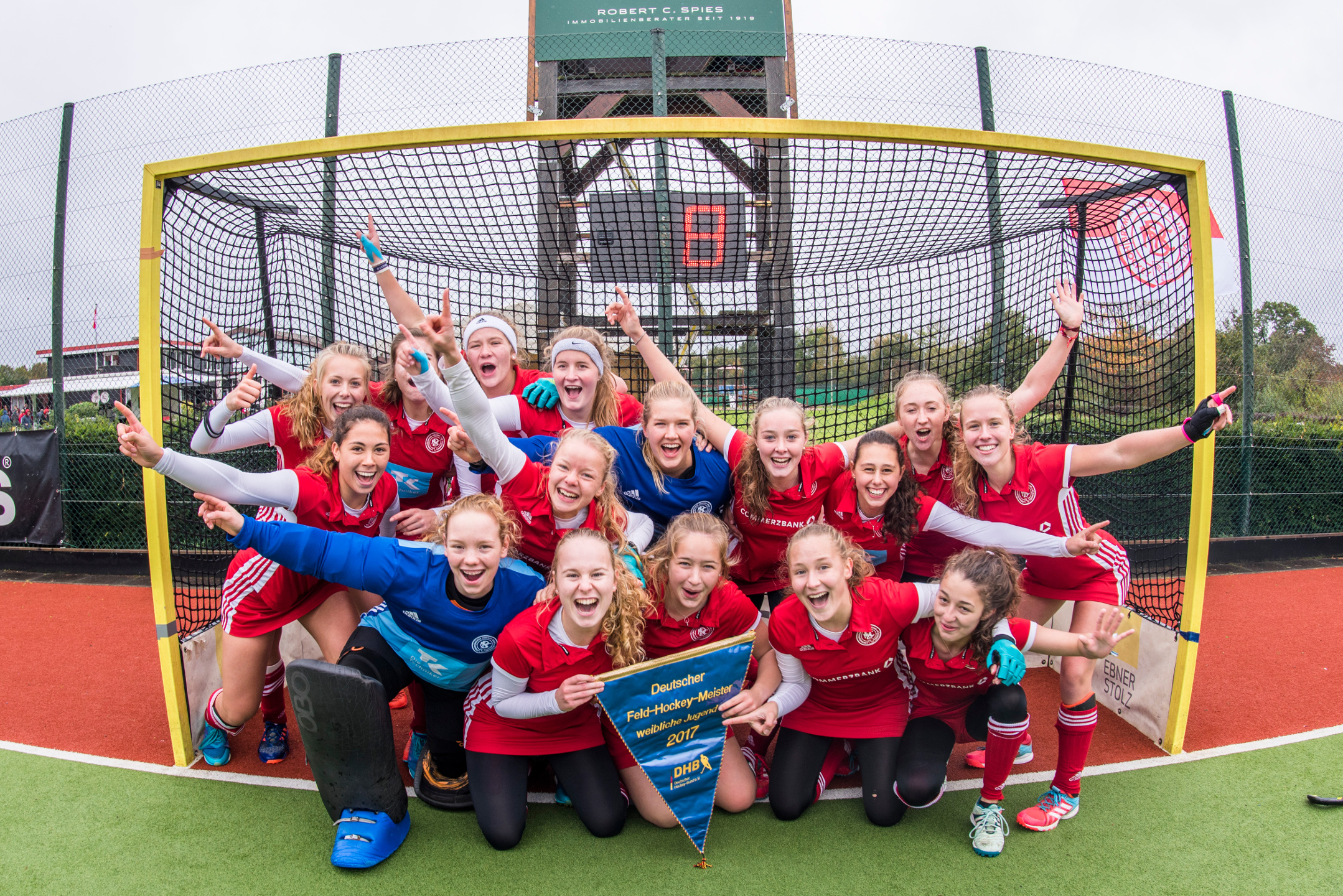 Die Damen-Mannschaft des BHC Eine fröhliche Frauen-Feldhockeymannschaft posiert jubelnd mit einem Siegerbanner vor dem Tor.