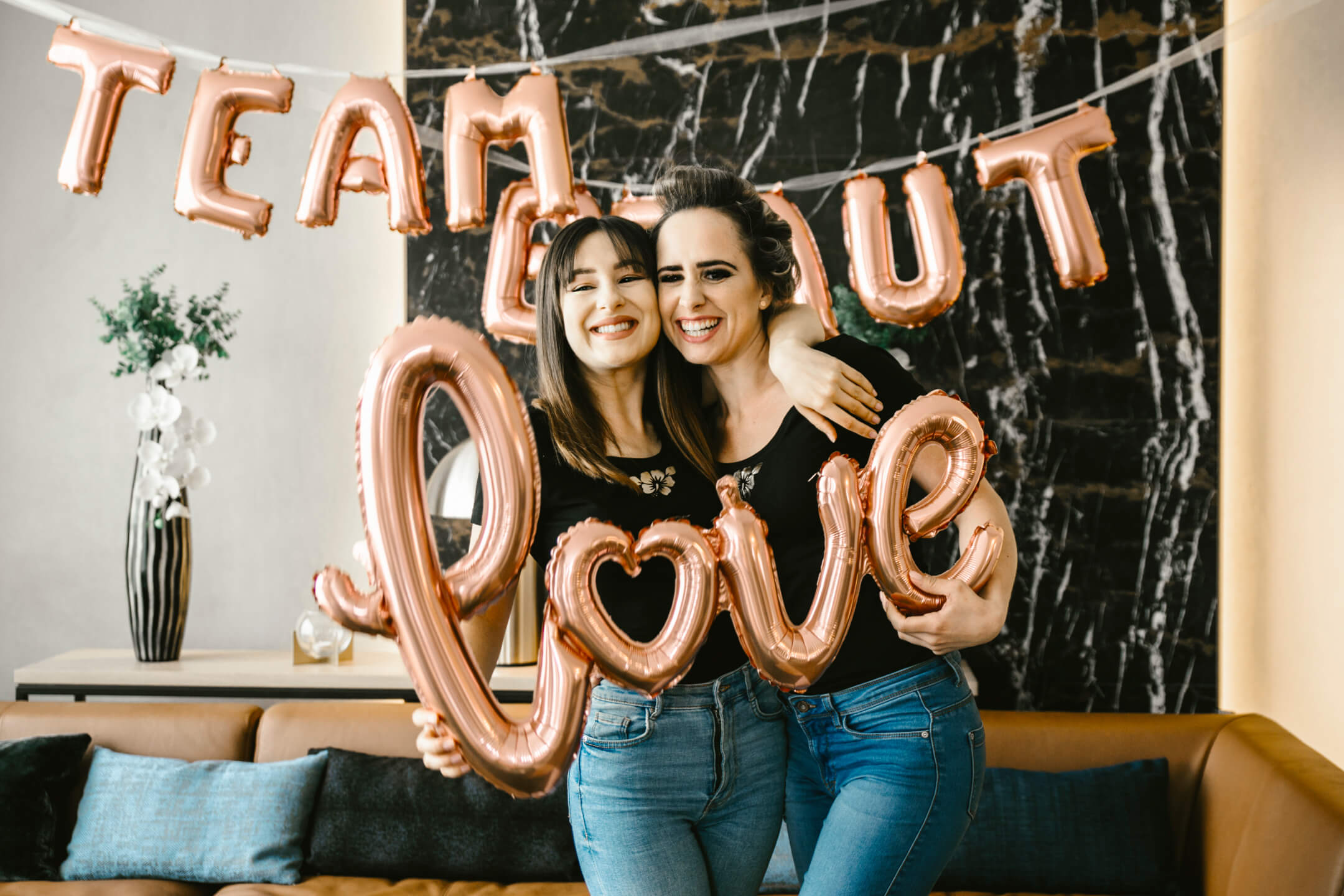 Porträtfoto Team Braut: Zwei Freundinnen der Braut präsentieren den Schriftzug "love" in Form eines Luftballons.