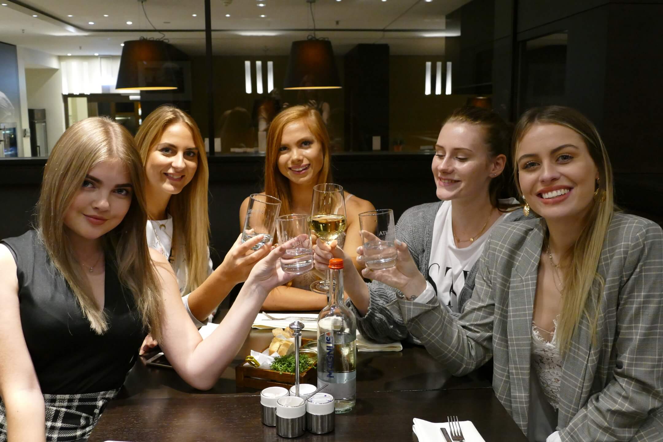 Fünf lächelnde Frauen stoßen mit Gläsern in einem stilvollen Restaurant an.