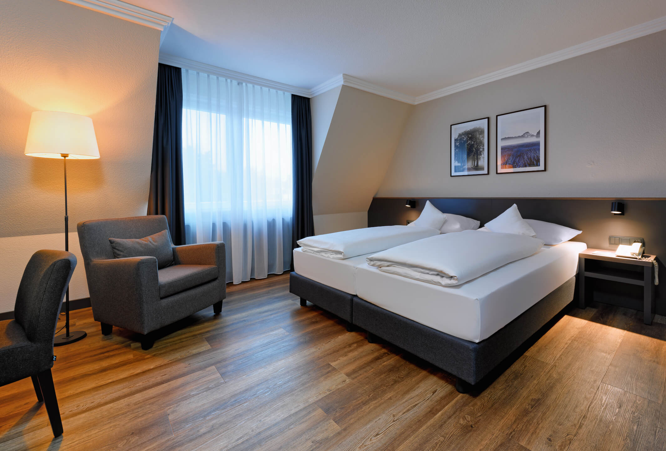 Bright hotel room with double bed, armchair, lamp and pictures on the wall, ATLANTIC Hotel Landgut Horn Bremen.