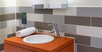 Modern washbasin with orange shelf, white washbasin, towel and gray wall tiles in the ATLANTIC Hotel.
