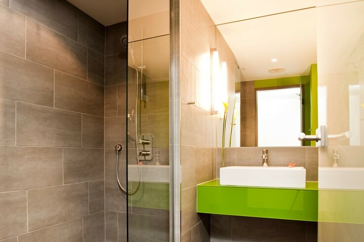 Modernes Badezimmer im ATLANTIC Hotel Kiel mit großer Dusche, grünem Waschbecken und stilvoller Beleuchtung.