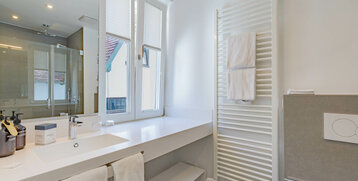 Modern bathroom with large mirror, washbasin, heated towel rail and glass shower at the ATLANTIC Grand Hotel Travemünde.