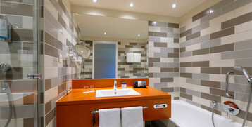 Modern bathroom with orange washbasin, mirror, shower and bathtub at the ATLANTIC Hotel Galopprennbahn.