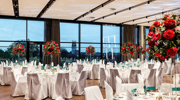 Festlich feiern im Engelsaal des ATLANTIC Hotel Münster Eleganter Bankettsaal im ATLANTIC Hotel Münster, mit runden, weiß gedeckten Tischen und üppigen Blumenarrangements.