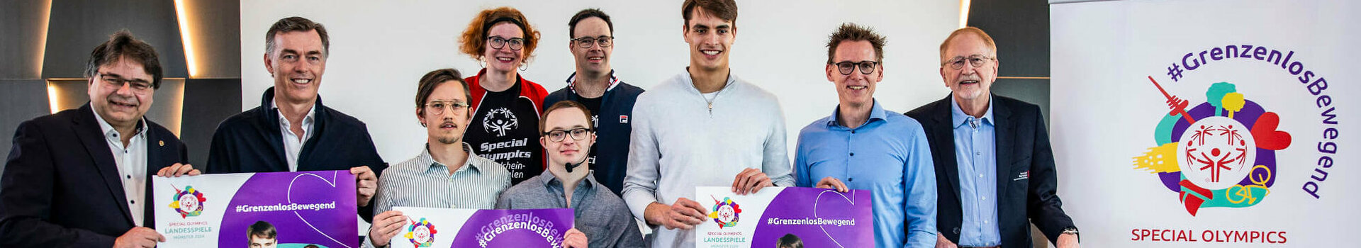 Gruppe von Menschen präsentiert Plakate für die Special Olympics Landesspiele Münster 2024 im ATLANTIC Hotel.