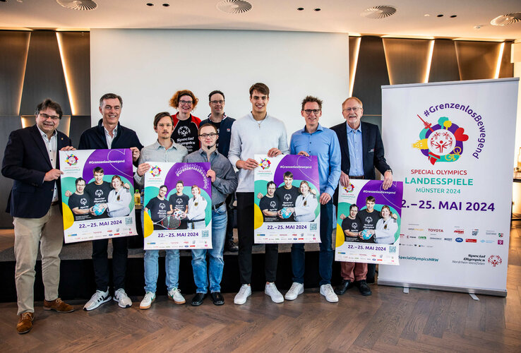 Gruppe von Menschen präsentiert Plakate für die Special Olympics Landesspiele Münster 2024 im ATLANTIC Hotel.