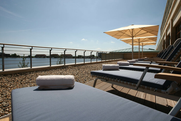 Sun terrace with loungers, parasols and a view of a lake on a clear day.