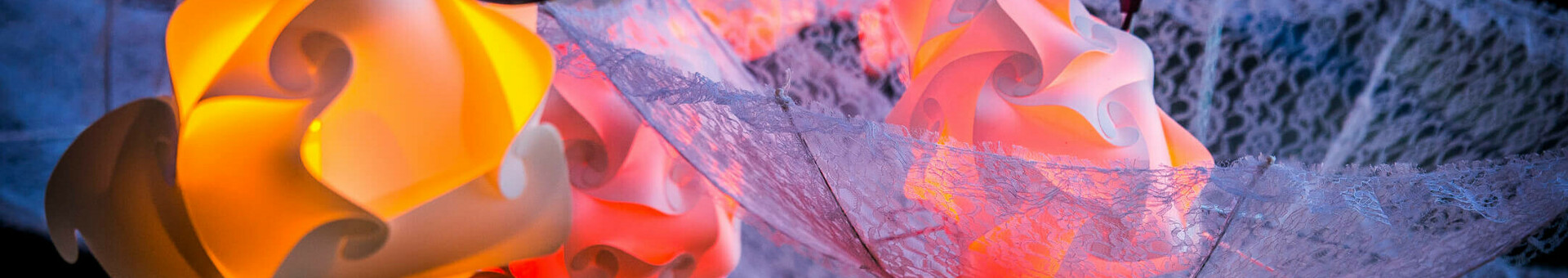 Travemünder Lichterzauber Bunte, dekorative Lampen hängen in kunstvollen Formen, umgeben von zarten Spitzenstoffen.