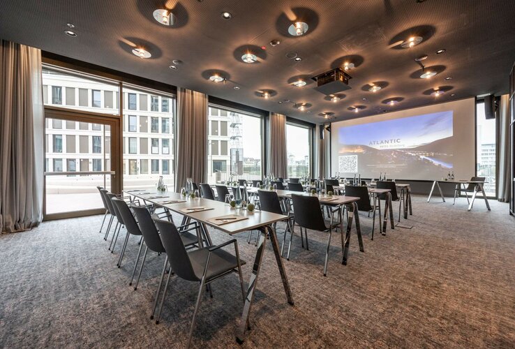 Lichtdurchfluteter Tagungsraum im ATLANTIC Hotel Heidelberg mit parlamentarischer Bestuhlung und großer Leinwand