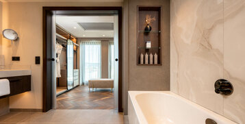 Modernes Badezimmer im ATLANTIC Hotel Heidelberg mit Badewanne, Regalen und Blick ins elegante Hotelzimmer.