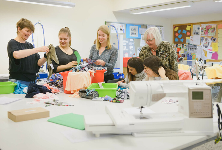 Group of women working creatively with fabrics in a bright room with a sewing machine.