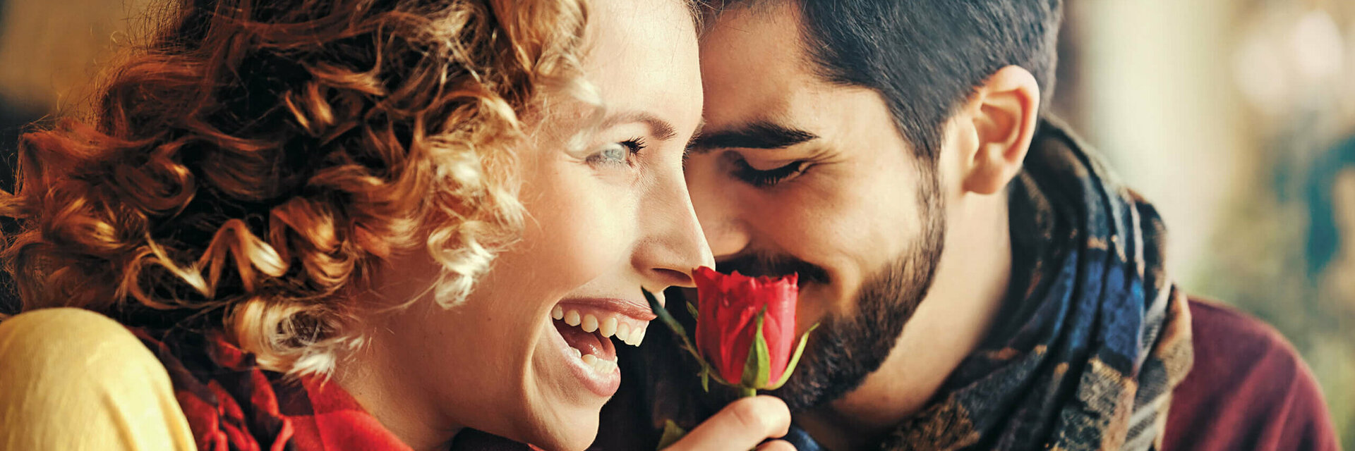 Ein lachendes Paar genießt eine rote Rose, symbolisiert Romantik und Freude im ATLANTIC Hotel Wilhelmshaven.