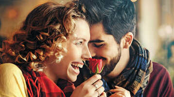 A laughing couple enjoying a red rose, symbolizing romance and joy at the ATLANTIC Hotel Wilhelmshaven.