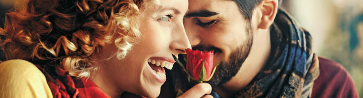 Ein lachendes Paar genießt eine rote Rose, symbolisiert Romantik und Freude im ATLANTIC Hotel Wilhelmshaven.