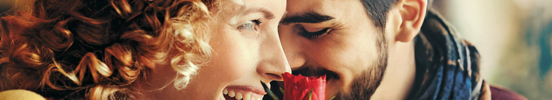 Ein lachendes Paar genießt eine rote Rose, symbolisiert Romantik und Freude im ATLANTIC Hotel Wilhelmshaven.