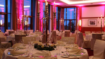 Celebrations Event room Wilhelmshaven | ATLANTIC Hotel Wilhelmshaven Elegant hotel restaurant with festively laid tables, candlesticks and atmospheric pink lighting.