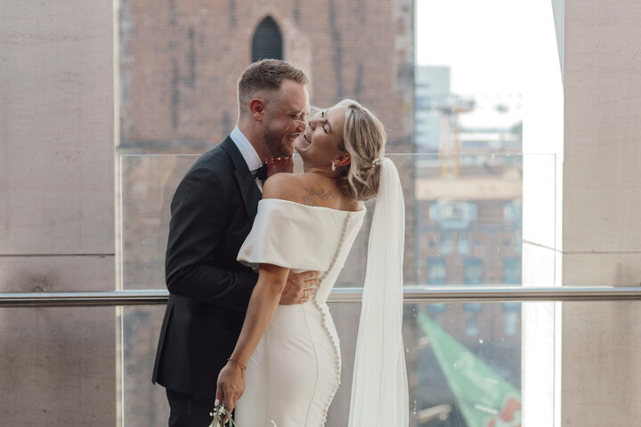 ATLANTIC Grand Hotel Bremen Hochzeit feiern Brautpaar lächelt sich auf einer Terrasse des ATLANTIC Grand Hotel Bremen an, im Hintergrund historische Architektur.