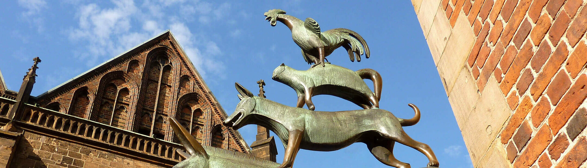 The Bremen Town Musicians Bronze statue of the Bremen Town Musicians in front of a historic brick façade, blue sky in the background.