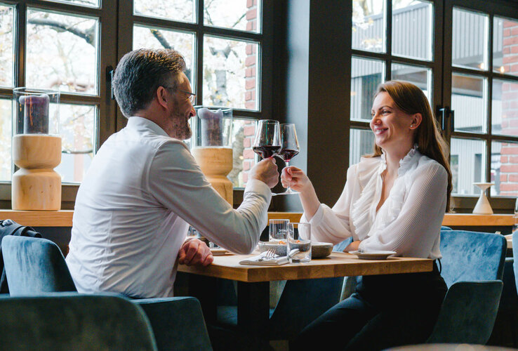 Paar stößt mit Weingläsern in elegantem Restaurant des ATLANTIC Hotel Landgut Horn an.