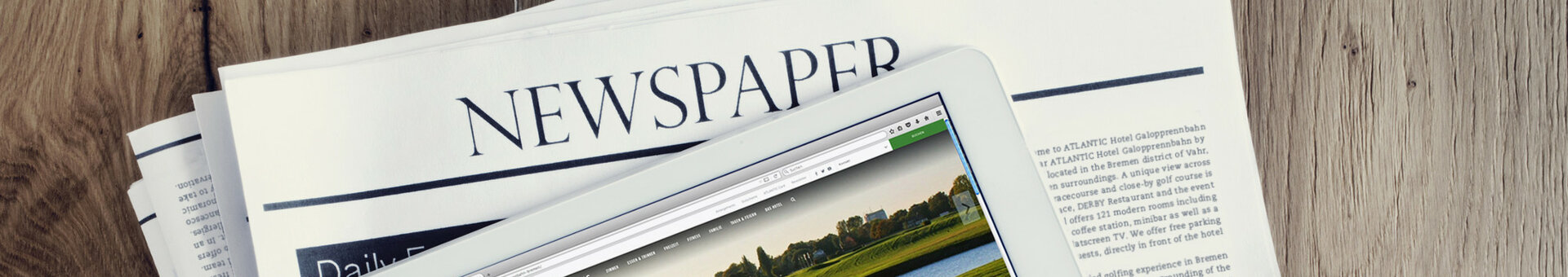 Tablet auf einer Zeitung, zeigt Hotelwebseite mit grünem Golfplatz. Holzuntergrund.