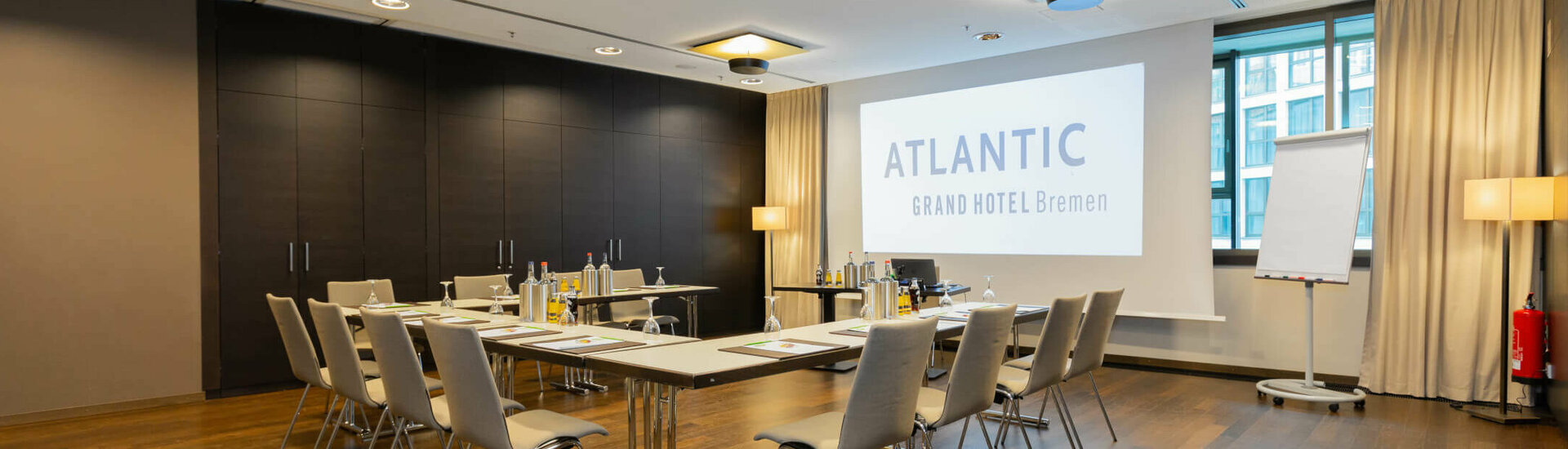 Modern conference room in the ATLANTIC Grand Hotel Bremen, with tables, chairs, projection screen and flipchart.