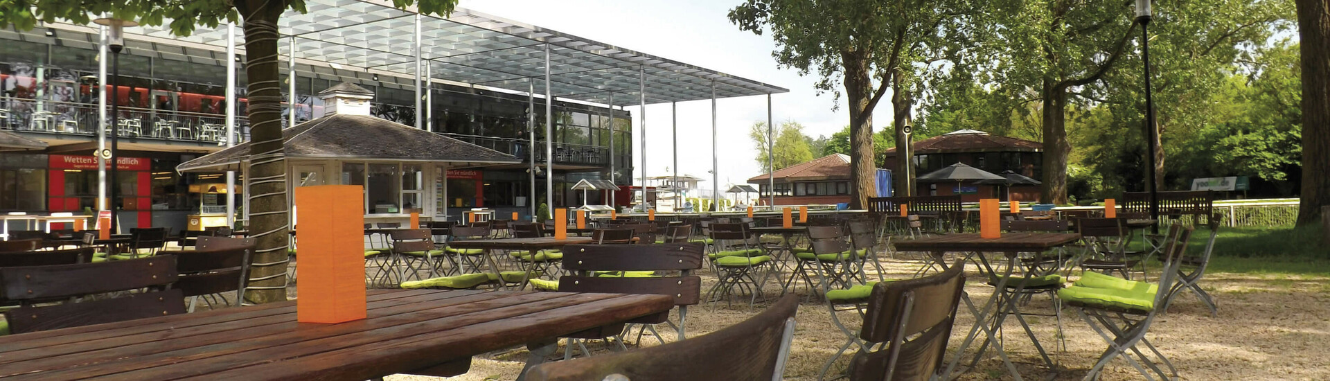 Außenterrasse des ATLANTIC Hotels mit Holztischen, grünen Kissen und Bäumen, im Hintergrund moderne Glasarchitektur.