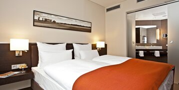 Modernes Hotelzimmer mit Doppelbett, oranger Decke, stilvollem Bad und Kunstwerk an der Wand im ATLANTIC Hotel Lübeck.